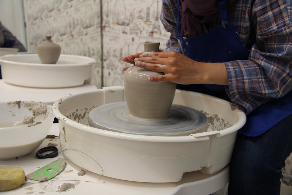 Artisan shaping a clay vase on a pottery wheel in an indoor studio.
